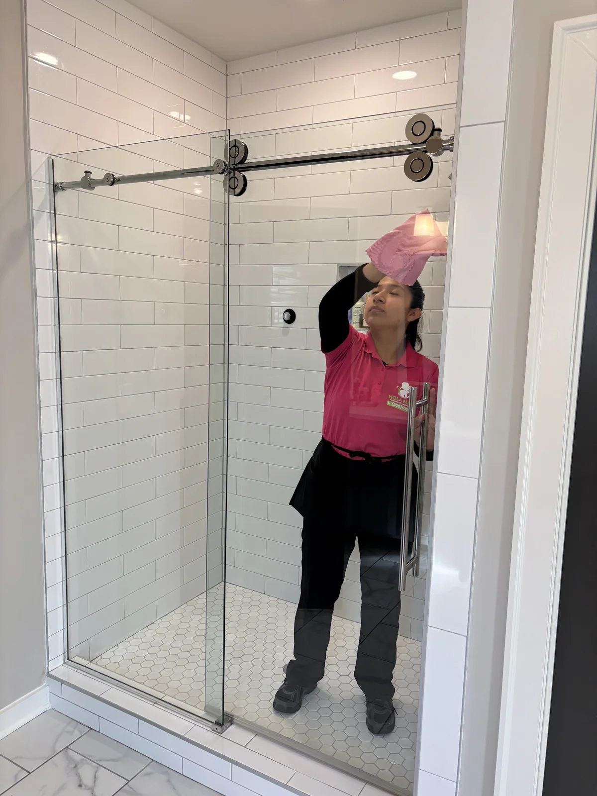 A Hola Maids team member cleaning the glass of a walk-in shower