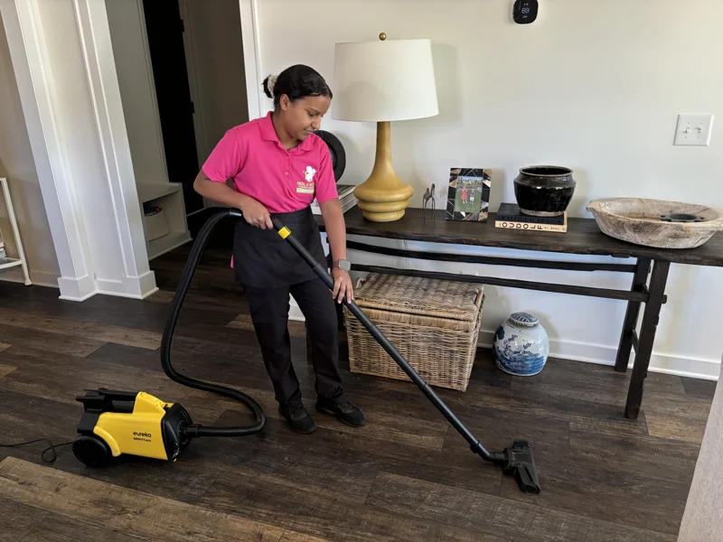 A Hola Maids team member vacuuming a dining area floor