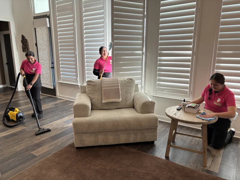 The Hola Maids team cleaning around a sofa and side table in a living room